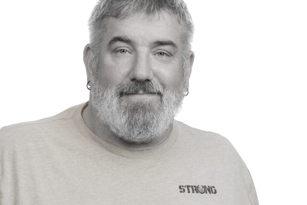 Studio portrait tight head and shoulders crop of bearded man with slight sepia tone.